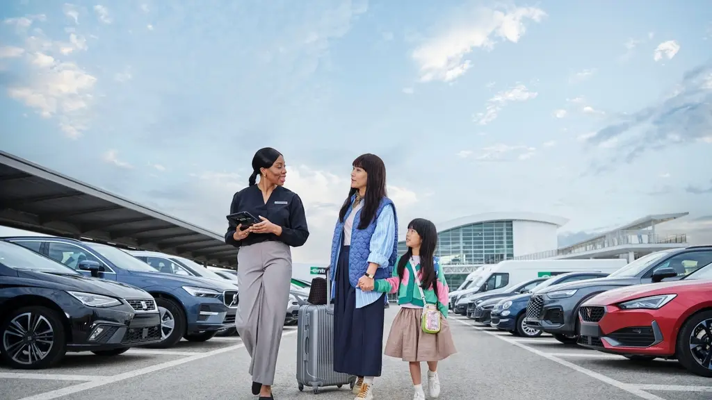 An Enterprise employee walks a traveling family with luggage to their rental vehicle