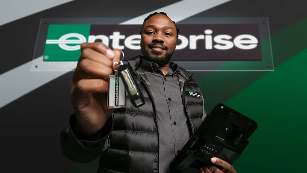An Enterprise employee holds out a set of keys in front of the green Enterprise sign