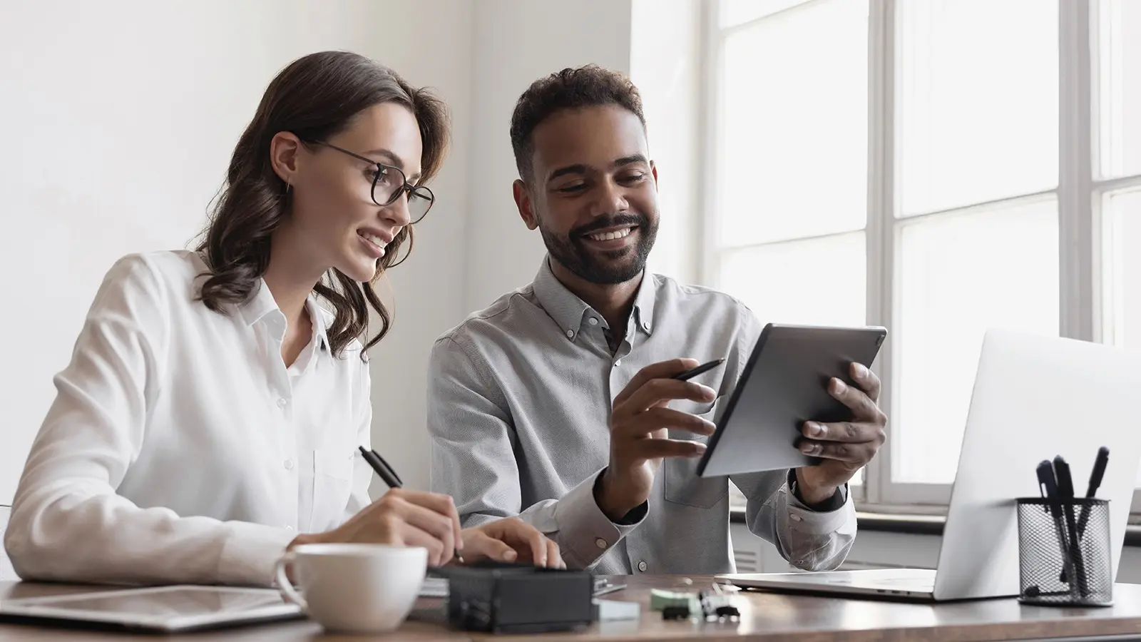 Two colleagues review a tablet together at a desk