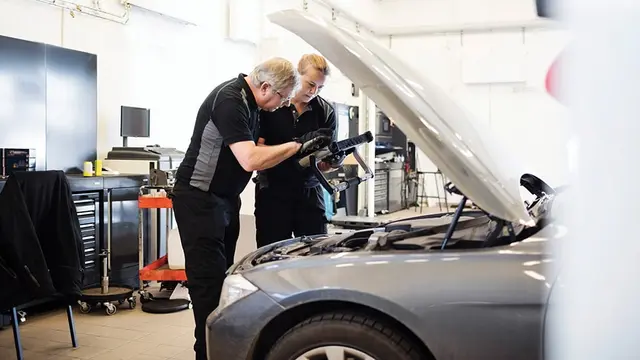 Service technicians review a vehicle with its hood open in a dealership service bay