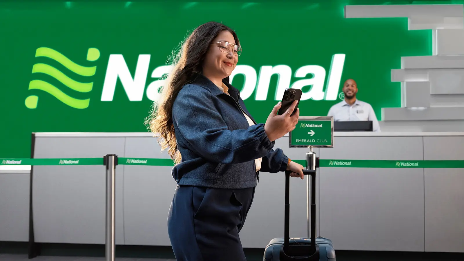 A business traveler with a rolling suitcase at a National Car Rental counter