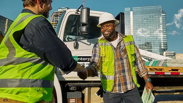 Two construction professionals in safety vests shake hands beside a work truck